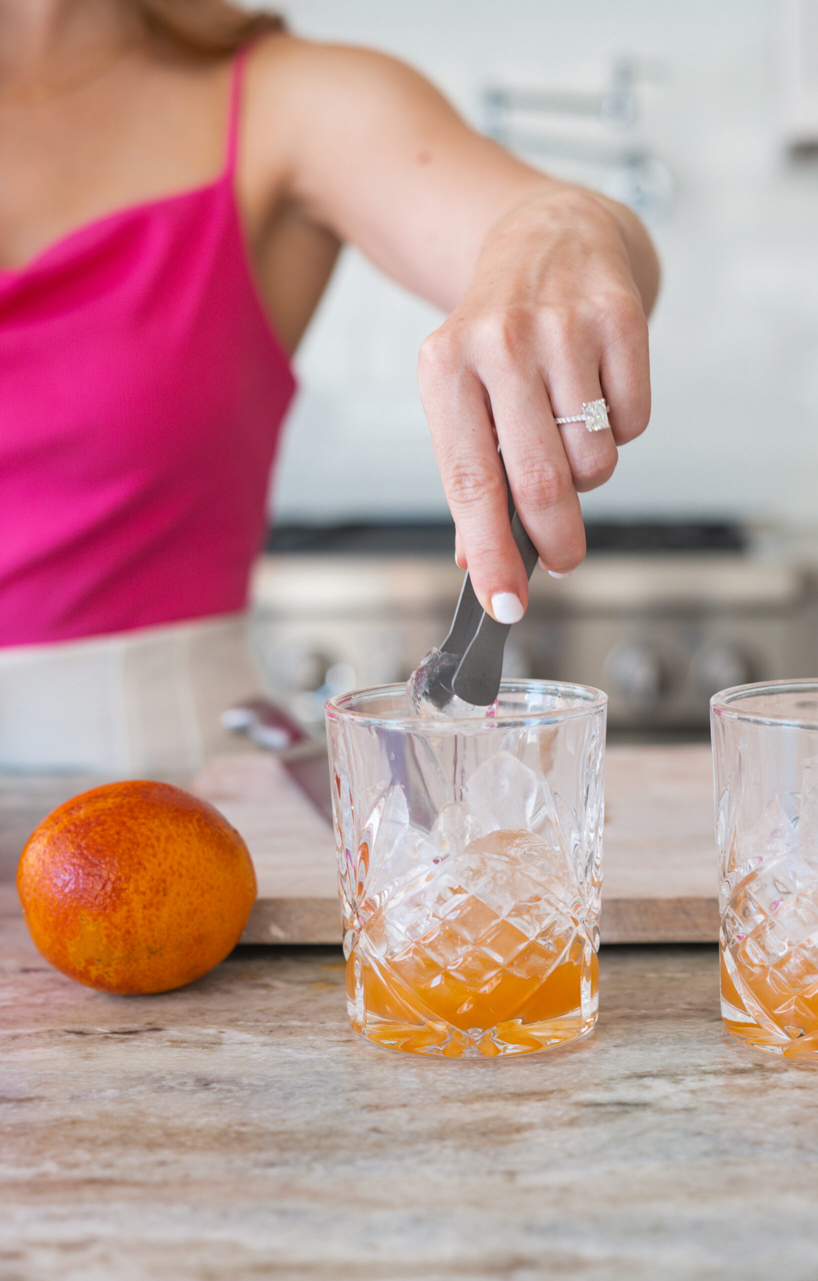 Girl holding tongs and placing an ice cube in a cocktail glass.
