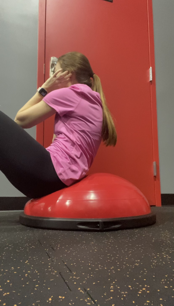 Female crunching forward on Bosu ball and twisting to the right so that her left elbow touches the outside of her right thigh. 
