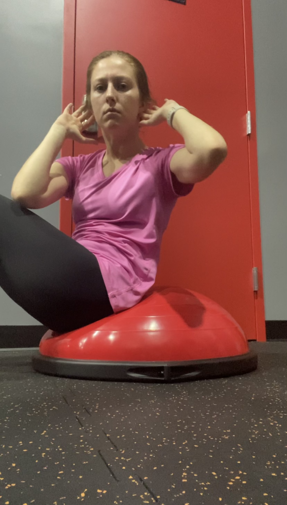 Female crunching forward on Bosu ball and twisting to the left so that her right elbow touches the outside of her left thigh. 